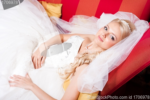 Image of beautiful  bride lying on red sofa