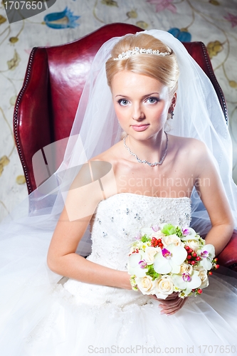 Image of beautiful  bride sitting in red armchair