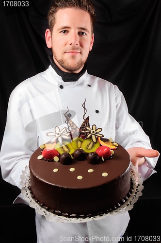 Image of Handsome chef with cake against dark background