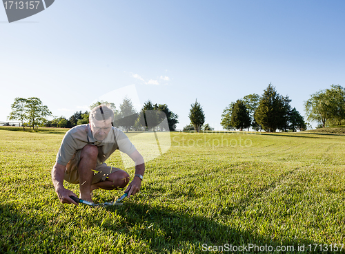 Image of Senior man cutting grass with shears