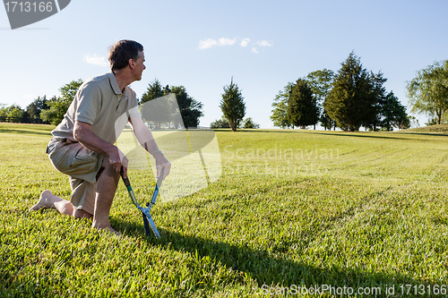 Image of Senior man cutting grass with shears