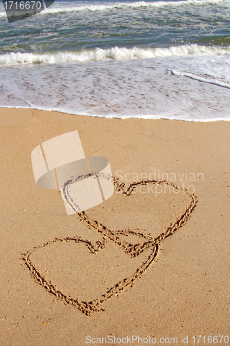 Image of handwritten heart on sand with wave approaching
