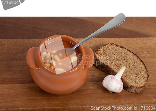 Image of Soup in ceramic pot with bread and garlic on wooden table