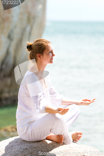 Image of Young woman practicing yoga by coast