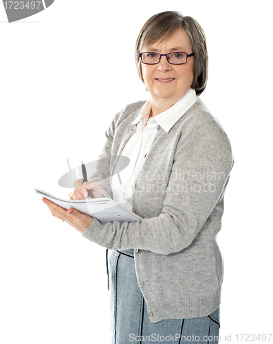 Image of Aged woman writing on spiral notebook