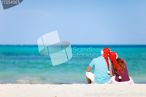 Image of Romantic couple in Santa hats sitting on tropical beach