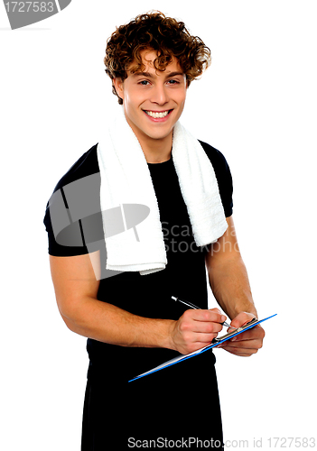 Image of Smiling male trainer writing on clipboard
