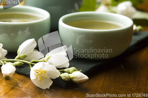 Image of Green tea with jasmine in cup and teapot on wooden table