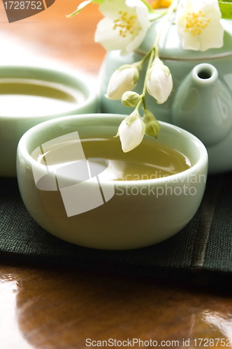 Image of Green tea with jasmine in cup and teapot on wooden table