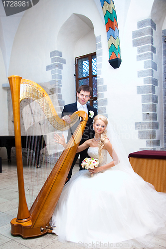 Image of groom and bride with harp in old town hall interior