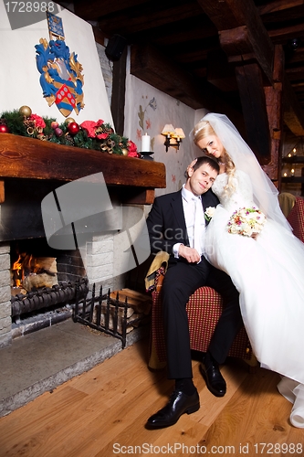 Image of beautiful groom and bride  sitting near fireplace