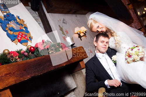 Image of beautiful groom and bride  sitting near fireplace