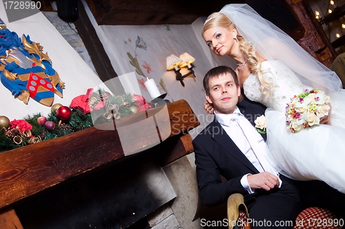 Image of beautiful groom and bride  sitting near fireplace
