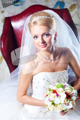 Image of beautiful  bride sitting in red armchair