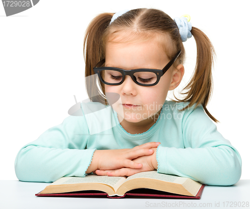 Image of Little girl reads a book while wearing glasses