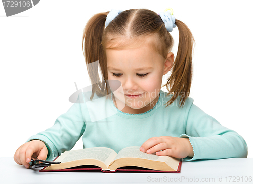 Image of Little girl reads a book while wearing glasses