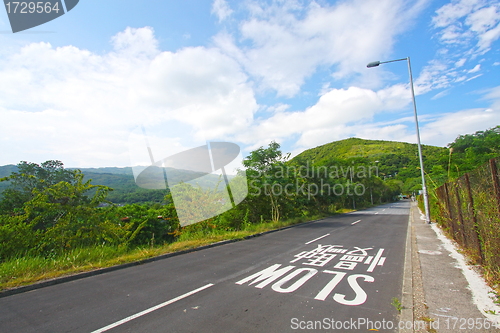 Image of Road in a meadow against the blue sky with white clouds 