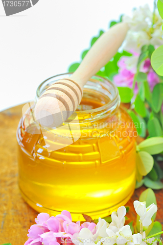 Image of glass jar full of honey and stick with acacia pink and white  fl