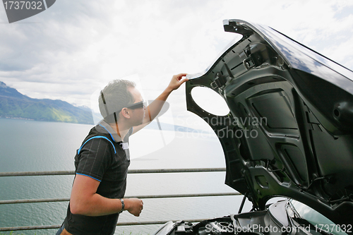 Image of man having a bad day checks his car to figure out what the probl