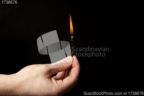 Image of Hand holding burning match stick on black background