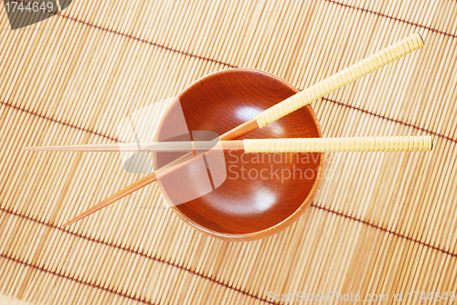 Image of Chopsticks with wooden bowl on bamboo matting background 