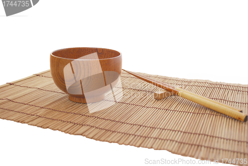 Image of Chopsticks with wooden bowl on bamboo matting background 