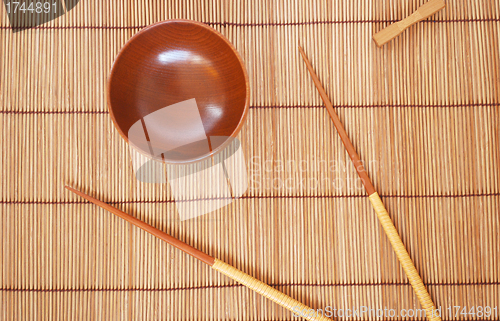 Image of Chopsticks with wooden bowl on bamboo matting background 