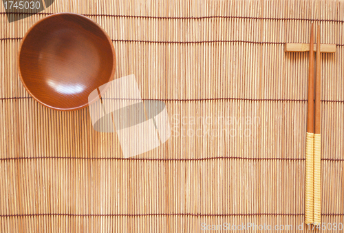 Image of Chopsticks with wooden bowl on bamboo matting background 