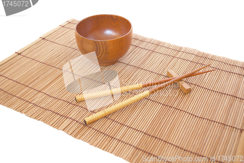 Image of Chopsticks with wooden bowl on bamboo matting background 