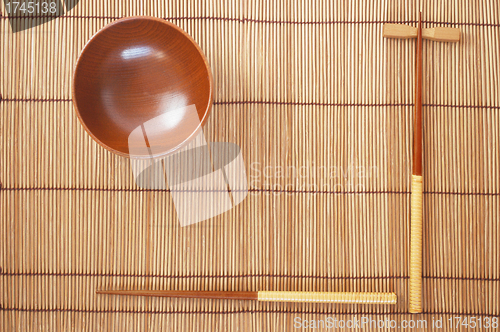 Image of Chopsticks with wooden bowl on bamboo matting background 