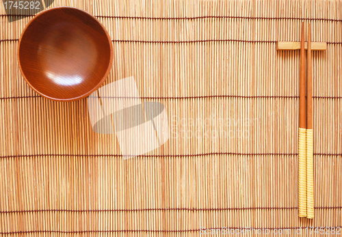 Image of Chopsticks with wooden bowl on bamboo matting background