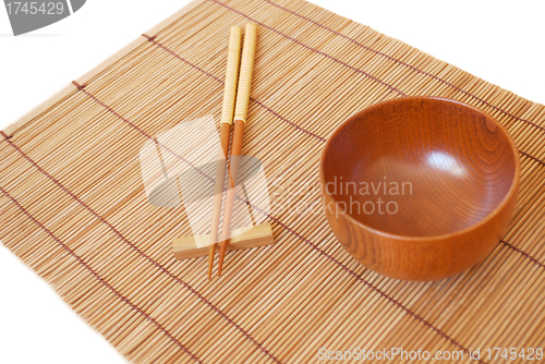 Image of Chopsticks with wooden bowl on bamboo matting background 