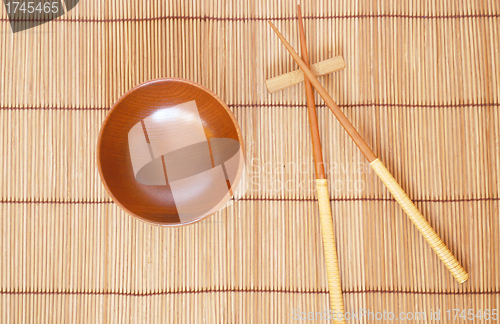Image of Chopsticks with wooden bowl on bamboo matting background 