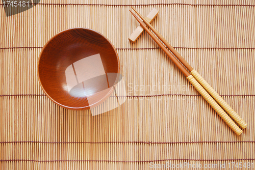 Image of Chopsticks with wooden bowl on bamboo matting background 
