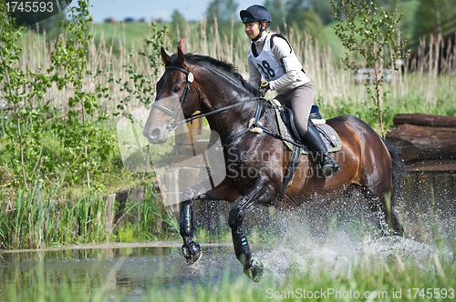 Image of Woman eventer on horse is run in Water jump