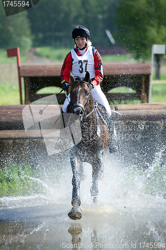 Image of Woman eventer on horse is run in Water jump