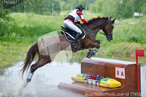 Image of Woman eventer on horse is overcomes the fence in water