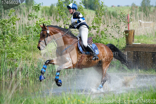 Image of Woman eventer on horse is run in Water jump