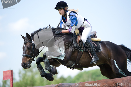 Image of Woman eventer on horse is overcomes the Log fence