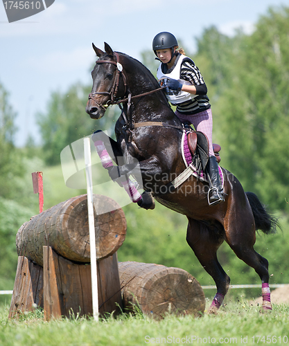 Image of Woman eventer on horse is overcomes the Log fence