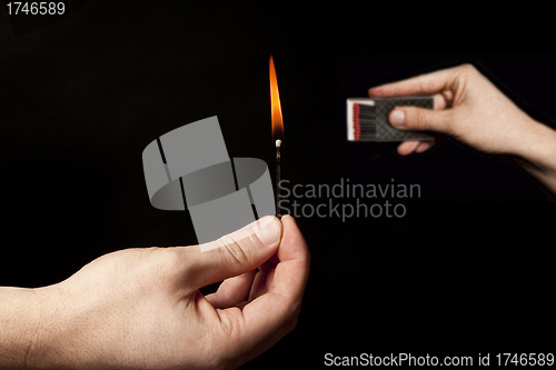 Image of Hand holding burning match stick on black background