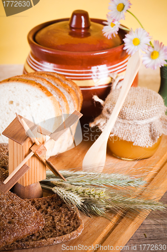Image of honey, flowers, spike and bread on table 