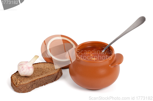 Image of Borsch in clay pot with bread and garlic
