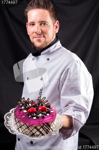 Image of Handsome confectioner with cake against dark background
