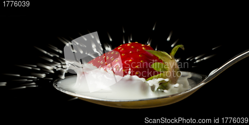 Image of red, ripe strawberry falling in spoon with milk