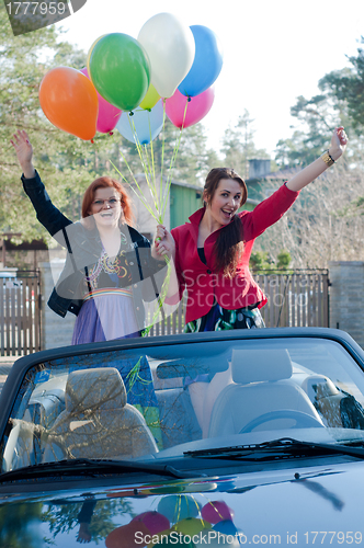 Image of Two young happy girls with air balloons in cabrio