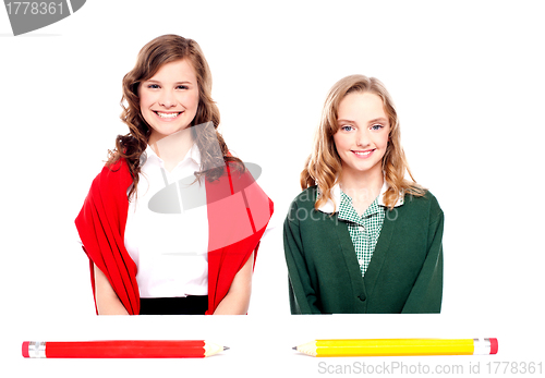 Image of Big pencils lying in front of two school girls