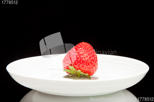 Image of white saucer with red strawberr on a black background