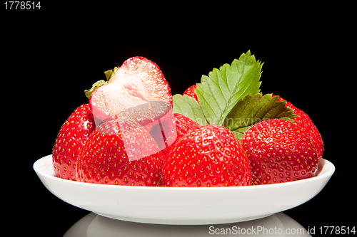 Image of white saucer with red strawberr on a black background