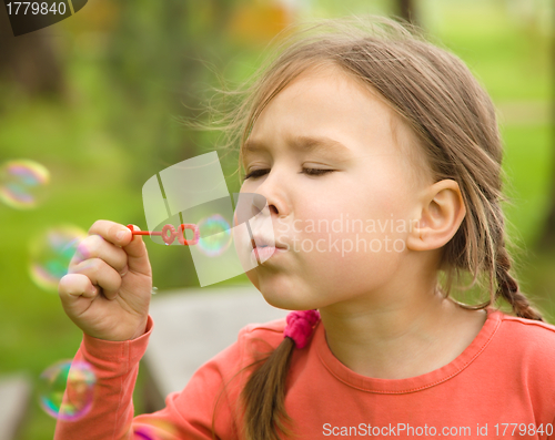 Image of Cute little girl is blowing soap bubbles